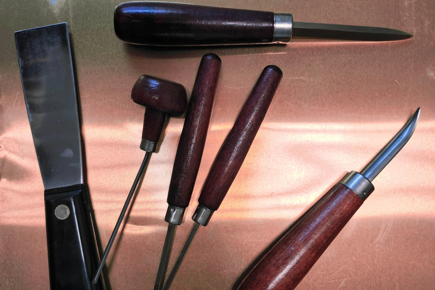 Scrapers, needles, and burnishers laid across a polished copper plate