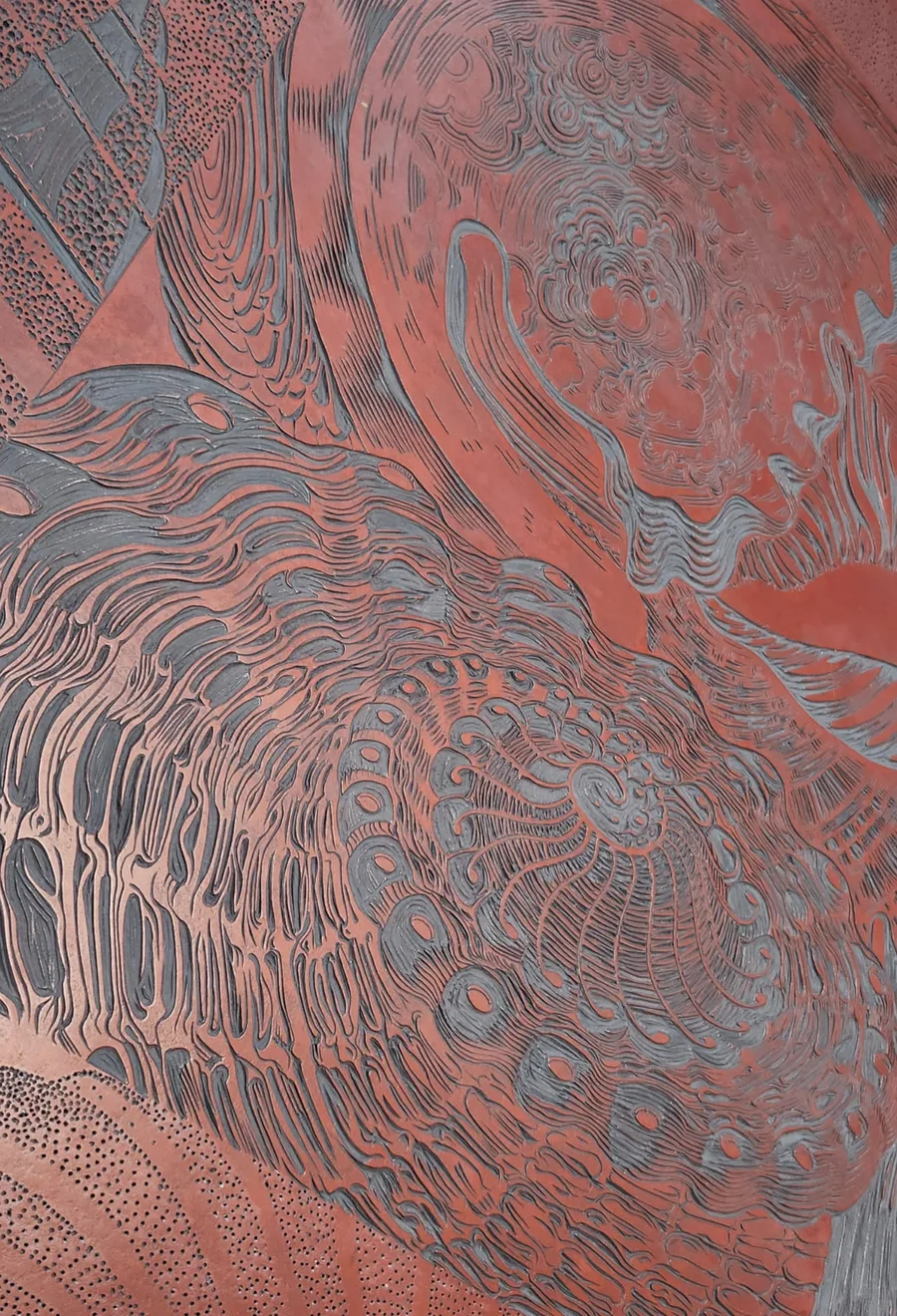 Close detail of a hand-worked copper plate, its surface cut with flowing etched lines in copper and grey tones